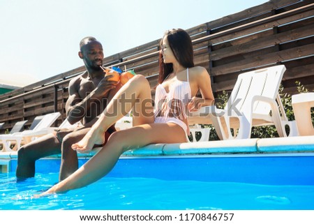 The african man and woman as friends playing and relaxing in a swimming pool during summer holidays. Happy people having fun by the pool. Leisure, swimming, summer, recreation, healthy lifstyle