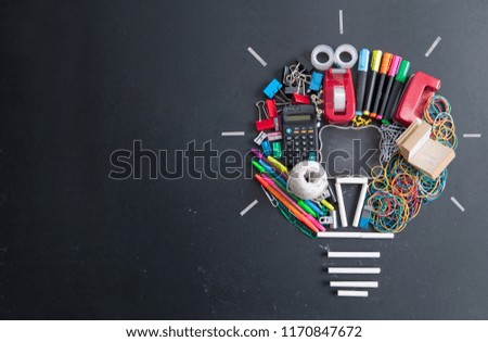 Light bulb shape made with many pieces of stationery on top of a chalkboard with space in the middle