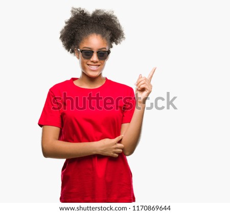 Young afro american woman wearing sunglasses over isolated background with a big smile on face, pointing with hand and finger to the side looking at the camera.