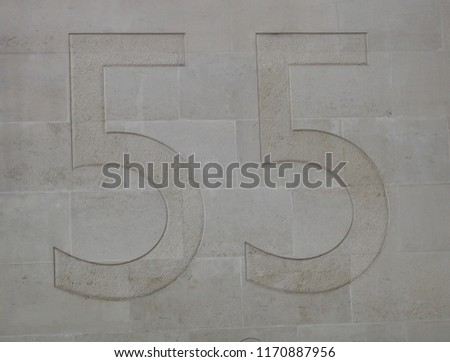 The Number 55 Subtly Etched In A Pale Beige Light Stone Block Wall Of A Building In The United Kingdom - Image