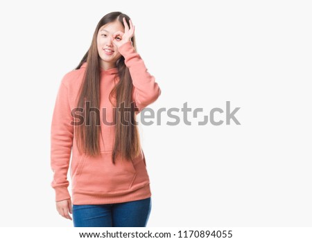 Young Chinese woman over isolated background wearing sport sweathshirt doing ok gesture with hand smiling, eye looking through fingers with happy face.