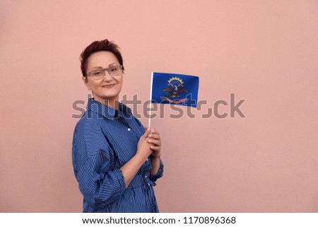 North Dakota flag. Woman holding North Dakota state flag. Nice portrait of middle aged lady 40 50 years old with a state flag over pink wall on the street outdoors.