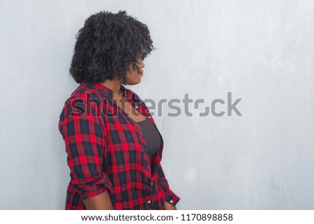 Young african american hipster woman over grey grunge wall looking to side, relax profile pose with natural face with confident smile.
