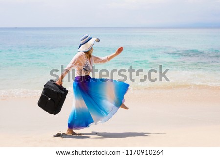 Care free woman walking with suitcase on the beach