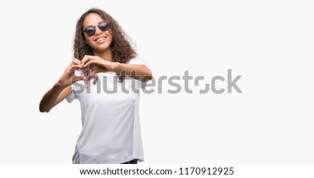 Young hispanic woman wearing sunglasses smiling in love showing heart symbol and shape with hands. Romantic concept.