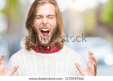 Young handsome man with long hair wearing winter sweater over isolated background celebrating mad and crazy for success with arms raised and closed eyes screaming excited. Winner concept