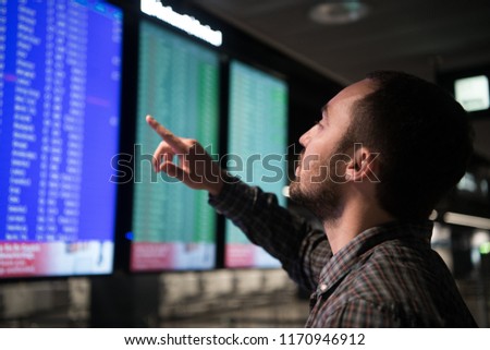 Young man traveling, pointing finger on train timetable in railway station