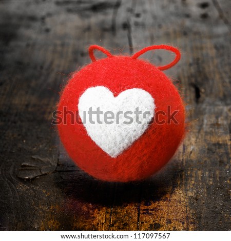 Colourful red textile Christmas bauble with a bold white heart design on an old grunge wooden table in square format for your seasonal or Valentines greeting