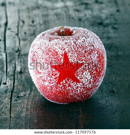 Decorative fresh ripe red Christmas apple frosted with a star pattern on an old vintage wooden table top, closeup in square format