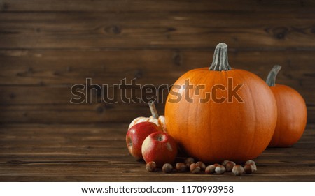 Autumn harvest still life with pumpkins, apples and hazelnuts on wooden background
