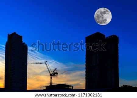 Silhouette two high buildings construction site and tower crane on blue sky and full moon at sunset time. Beautiful background and copy space.