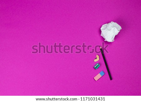 A flat lay photo of stationery set: pencil, rubber, sharpener and crumpled paper ball on the pink background on the table in the office or school or university. Workspace of student or office worker.