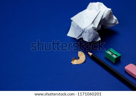 A closeup photo of stationary set: pencil, rubber, sharpener, crumped paper ball and notebook  on the blue background on the table in office,school or university. Workspace of student or office worker