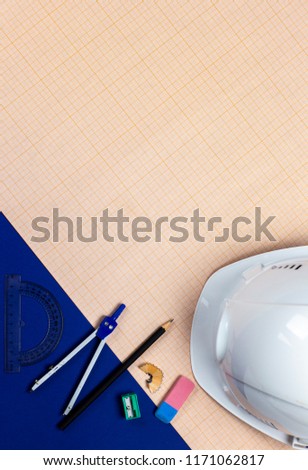 A stylish flat lay photo of stationery set and a white helmet on the blue background and graph paper. A great photo of architect's hard work.