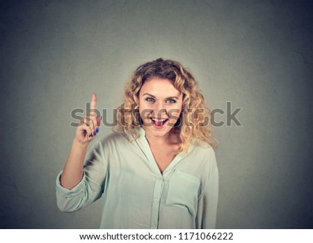 Portrait of a casual woman holding finger up having bright idea on gray background