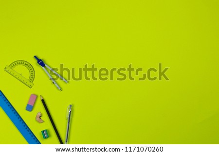 A photo of stationery set: pencil, rubber, sharpener, compass, protractor, ruler, crumpled paper ball and etc. on the yellow background on the table . Workspace of student or office worker.