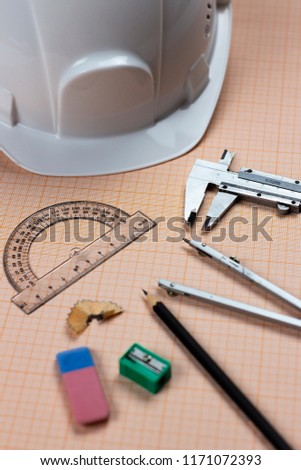 A close-up photo of stationary set and white helmet on the background of graph paper on the table or desk in office or university. A great photo of architect's work.