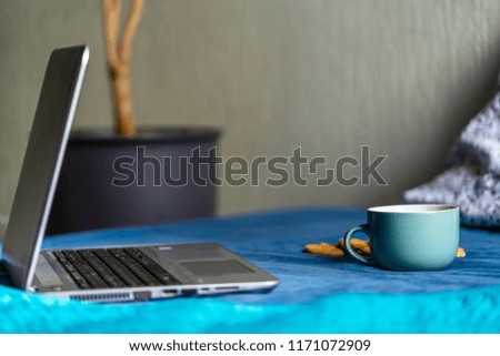 Tea with Lemon and Cookies with Chocolate Laying on Mattress - Grey Laptop Besides it, Blurred Turquoise Background