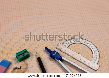A close-up photo of stationary set: pen, pencil, compass, rubber, protractor, calipers and etc. on the graph paper background on the table in office, school or university. A workspace of student.