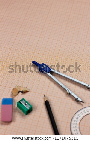 A close-up photo of stationary set: pen, pencil, compass, rubber, protractor, calipers and etc. on the graph paper background on the table in office, school or university. A workspace of student.