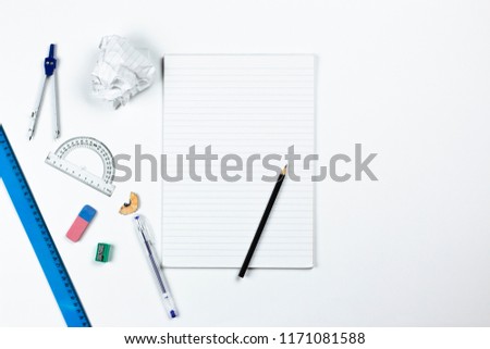 A photo of stationery set: pencil, rubber, sharpener, compass, protractor, ruler and crumpled paper ball on the white background on the table . Workspace of student or office worker.