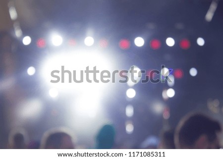 unfocused blurred and illuminated concept shot from music event in performance time with crowd of people near stage in twilight time with light glares 