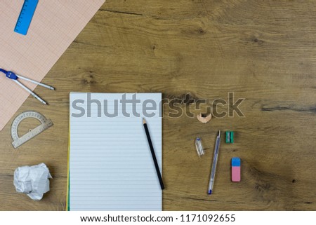 A photo of stationery set: pencil, rubber, sharpener, compass, protractor, ruler and crumpled paper ball on the wooden background on the table . Workspace of student or office worker.