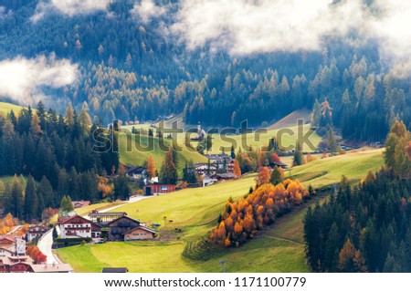 Amazing aerial autumn view on alpine town, sunlit meadows under low clouds. Location place: Santa Maddalena (Santa Magdalena), South Tyrol, Dolomite Alps, Italy. Royalty-Free Stock Photo #1171100779