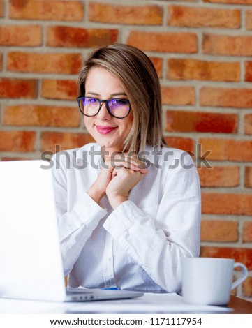 Young businesswoman sitting on a table with laptop computer and cup of coffee. Brick wall on background