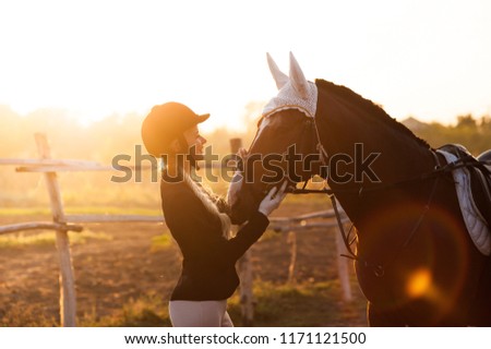 beautiful girl stands with a horse in the rays of a setting sun
