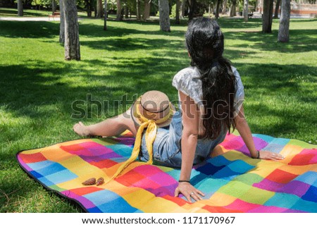 Beautiful young woman sitting on a colorful blanket in the park.