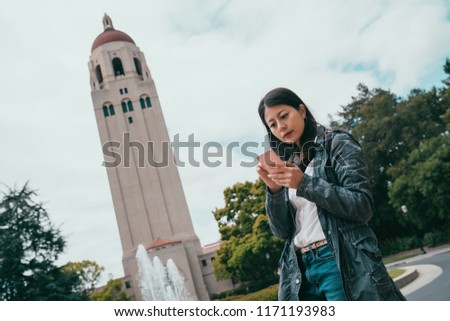 female aisan exchange student searching on phone while taking a break in her beautiful school.