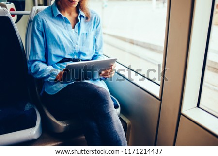 Cropped image of young woman using digital tablet and free wifi connection in tram while getting to job, female checking banking balance on portable pc typing information sitting in public transport