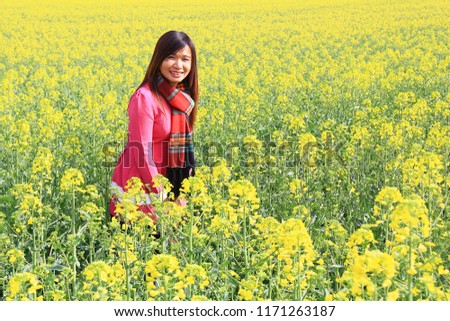 Pretty Asian tourist in red dress at the yellow flower field background.