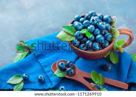 Blueberries in a ceramic cup with wooden spoons and a linen napkin. Ripe and sweet summer berries on a stone background. Neutral colors, blue and gray palette, copy space