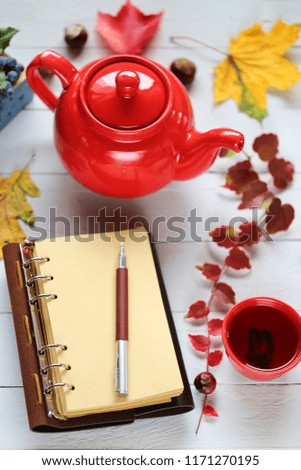 Autumn Mockup.Empty notebook with red kettle and cup with tea, tray with mahonia,  yellow oak and maple leaves on a wooden blue board background.Autumn tea. Autumn time