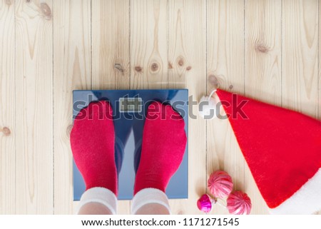 Female feet standing on electronic scales for weight control in red socks with Christmas decoration