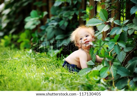 Happy baby sitting in green grass. He smiles and laughs. Hot summer day.