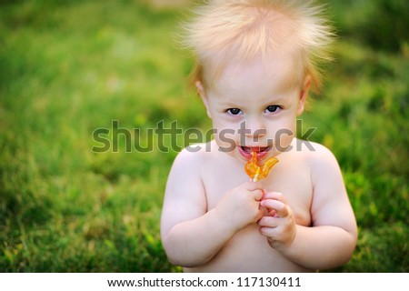 Happy kid with fluffy blond hair has a sweet candy. He looks and laughs.