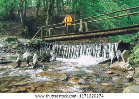 young adult man sitting at wooden bridge cross mountain river. travel concept