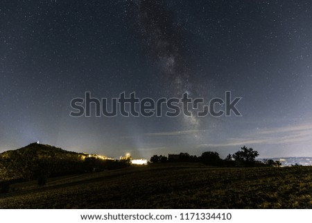 Beautiful view of starred night sky with milky way over a cultivated field Assisi town (Umbria, italy) in the background