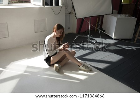 Model sits on the floor and uses a smartphone in a professional photo studio.