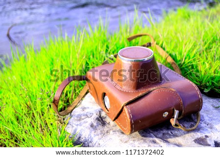 lying on a stone old camera around him growing green grass and flowing river. Travel to nature with a film camera