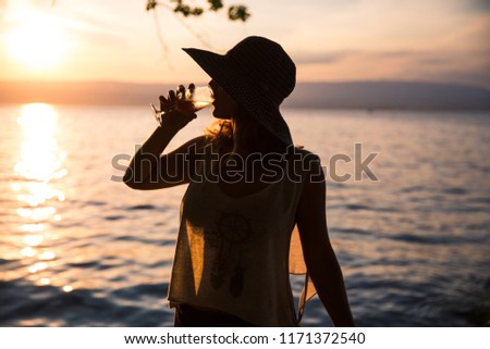 Silhouetted Woman Drinking a Glass of Rosé Wine and Wearing a See-through Summer T-Shirt at Sunset Royalty-Free Stock Photo #1171372540