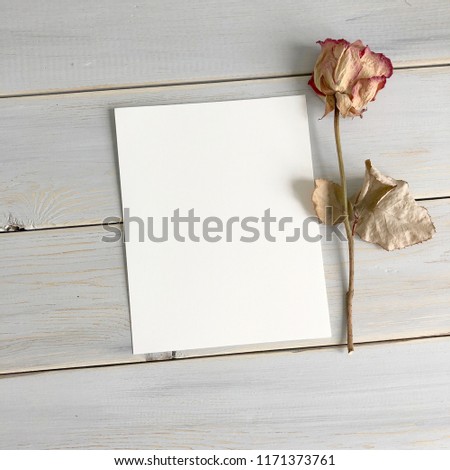 white sheet of paper and a rose on a wooden background
