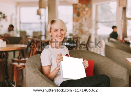 Young happy woman sitting in restaurant and holding photo album
