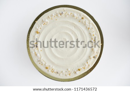 Cake with white cream, decorated with silver and gold confectionery sprinkles and gold leaf on a white background. Picture for a menu or a confectionery catalog. Top view.