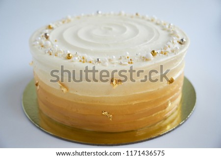 Cake with white cream, decorated with silver and gold confectionery sprinkles and gold leaf on a white background. Picture for a menu or a confectionery catalog.