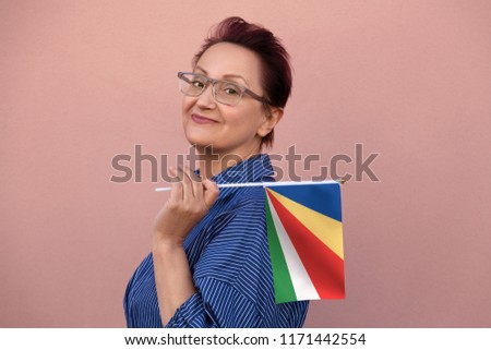 Seychelles flag. Woman holding Seychelles flag. Nice portrait of middle aged lady 40 50 years old with a national flag over pink wall background outdoors.