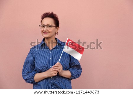 Singapore flag. Woman holding Singapore flag. Nice portrait of middle aged lady 40 50 years old with a national flag over pink wall background outdoors.